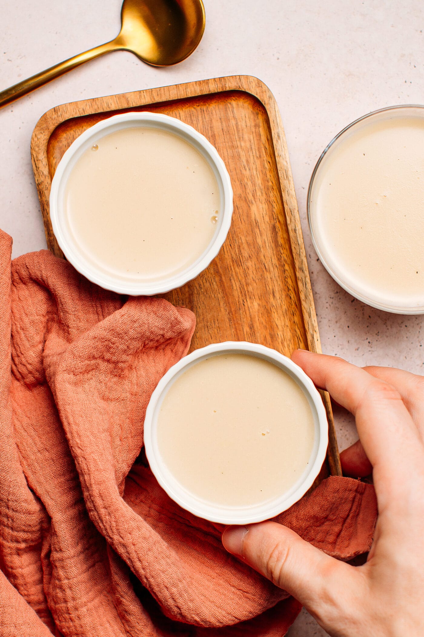 Two ramekins with panna cotta on a wooden board.