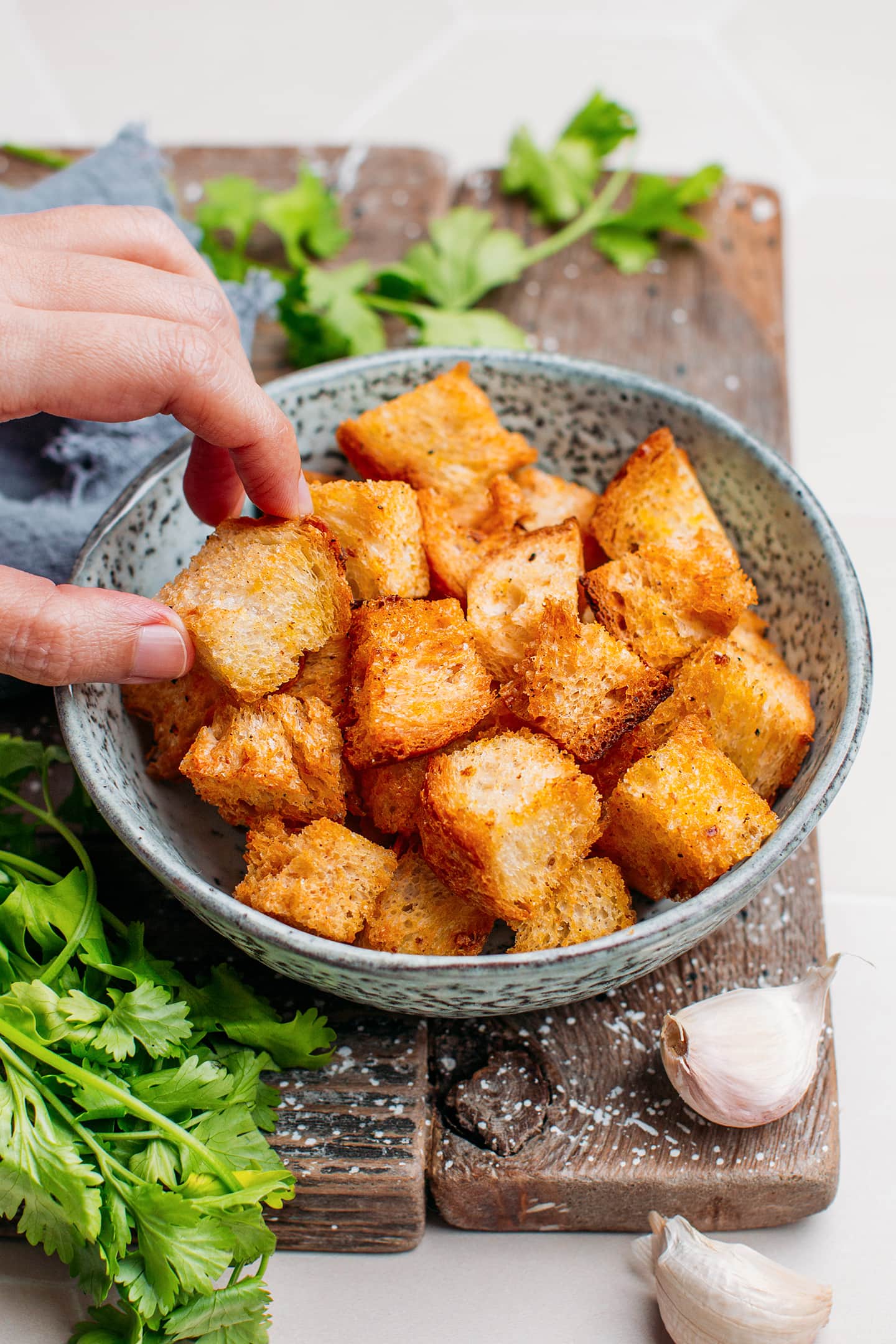 Hand holding a piece of crouton over a serving bowl.