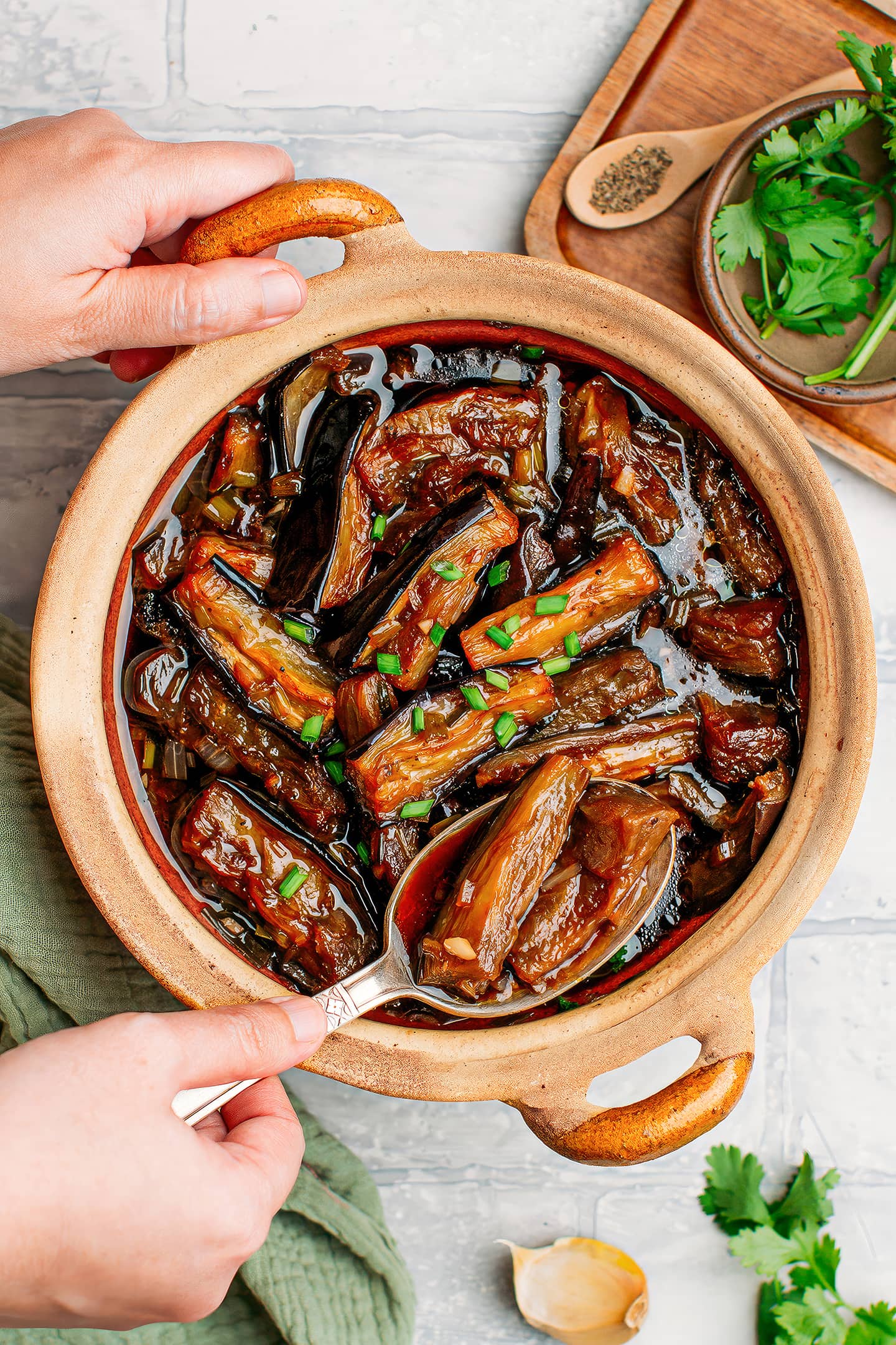 Holding a clay pot filled with braised eggplants.