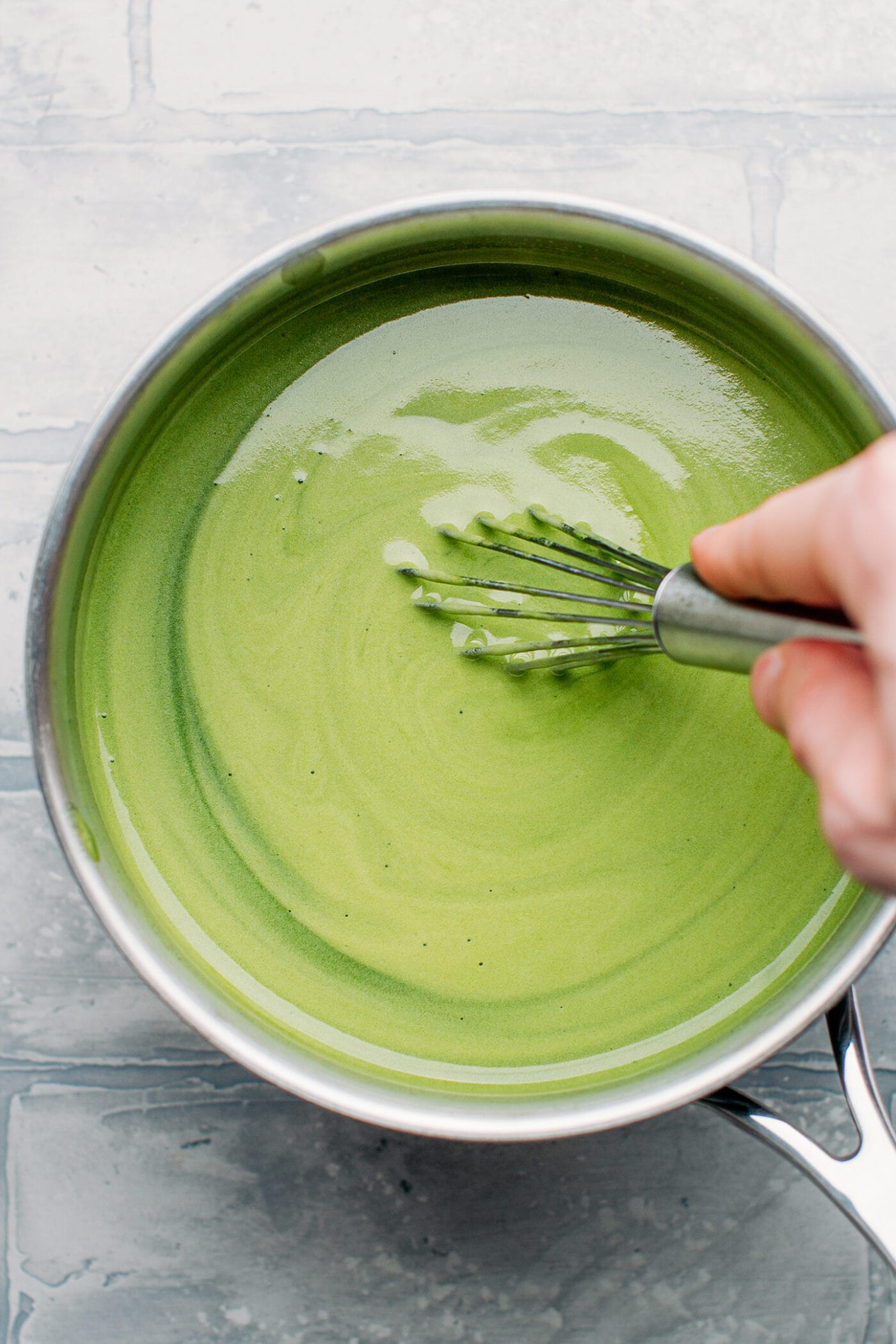 Whisking matcha milk in a saucepan.