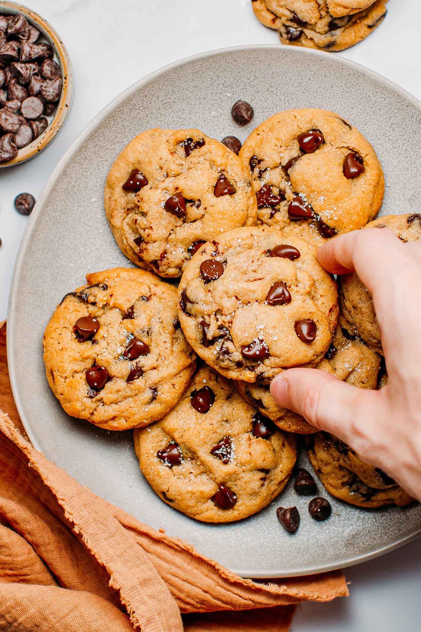 Hand taking a chocolate chip cookie out of a plate.