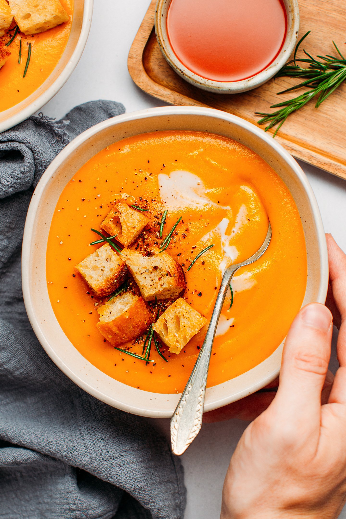 Bowl of sweet potato soup topped with croutons and rosemary.