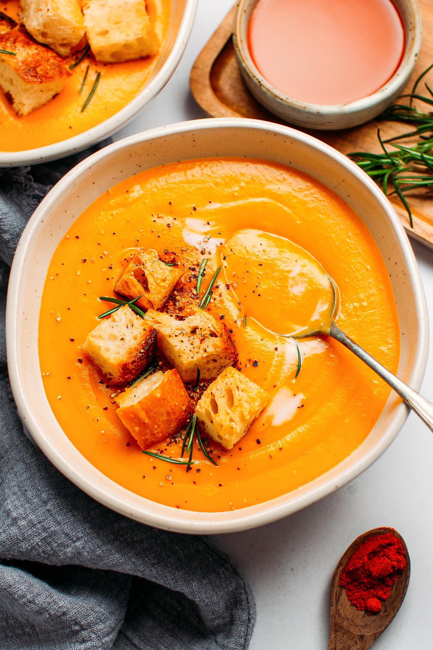 Bowl of sweet potato soup topped with croutons and rosemary.