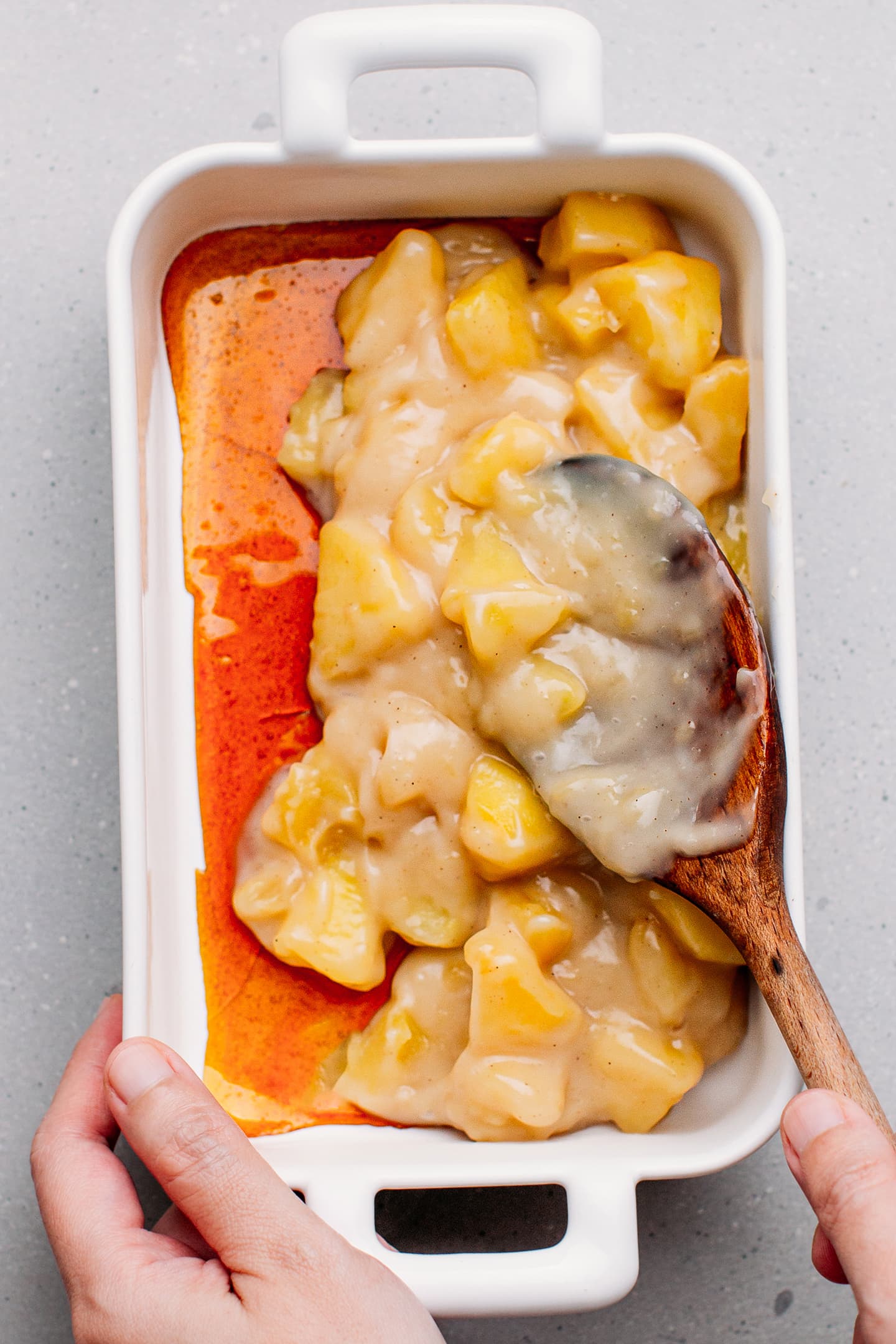 Pouring flan and apples over caramel in a baking dish.