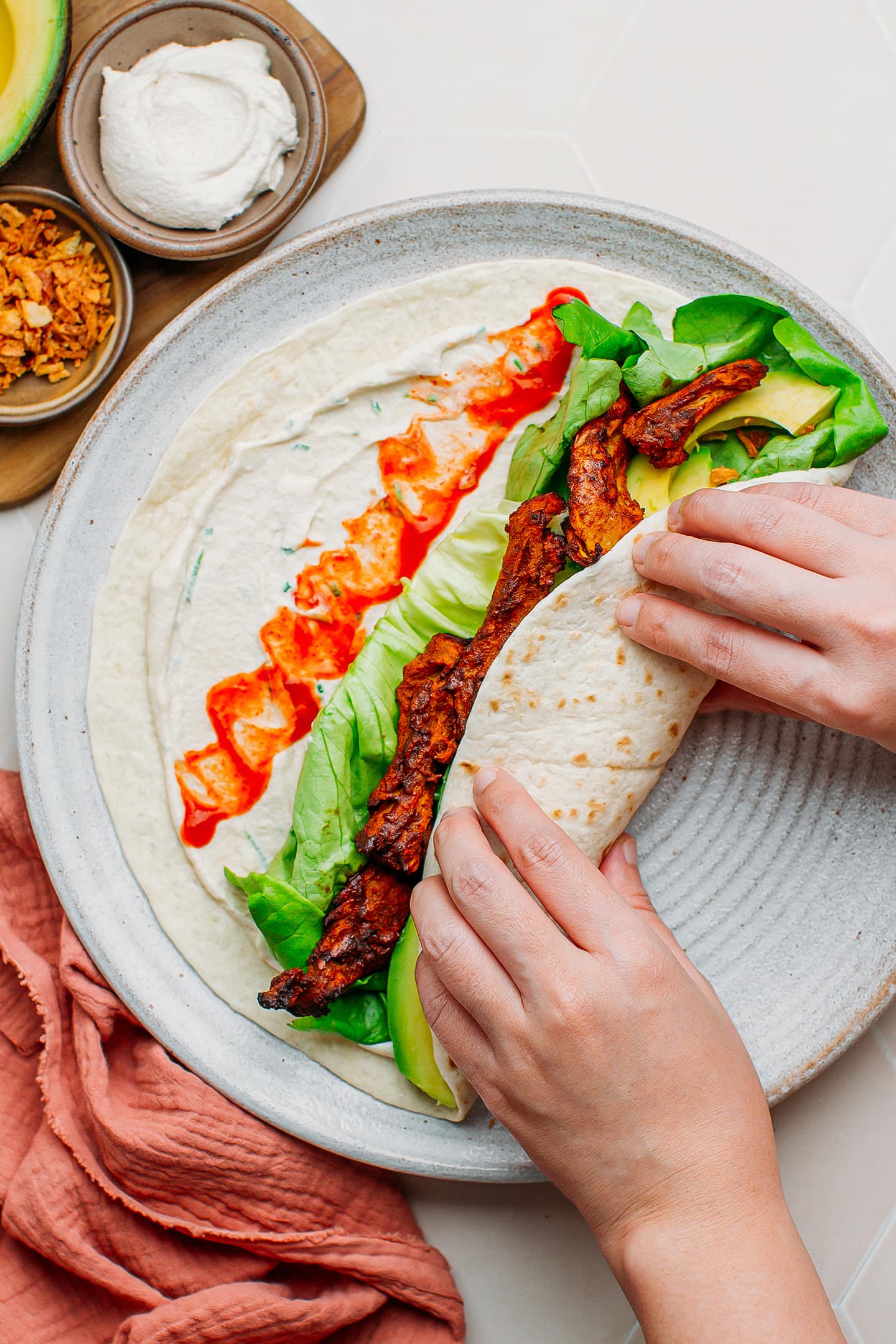 Rolling a tortilla wrap containing lettuce and vegan chicken.