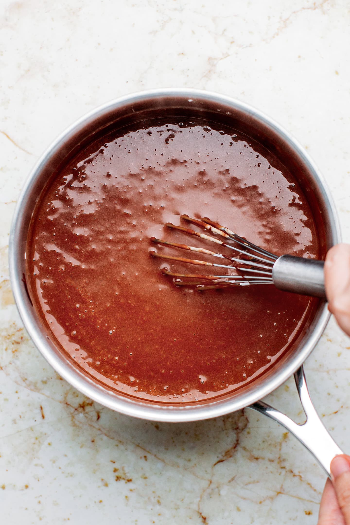 Whisking melted dark chocolate and milk in a saucepan.