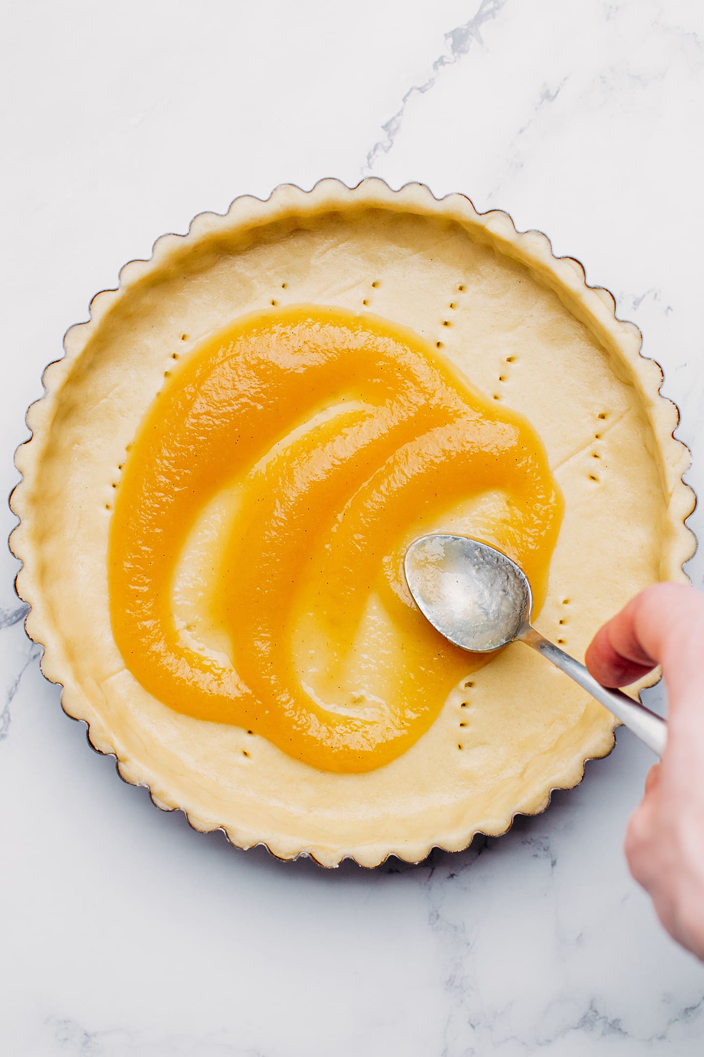 Spreading apple sauce on top of a pie crust.